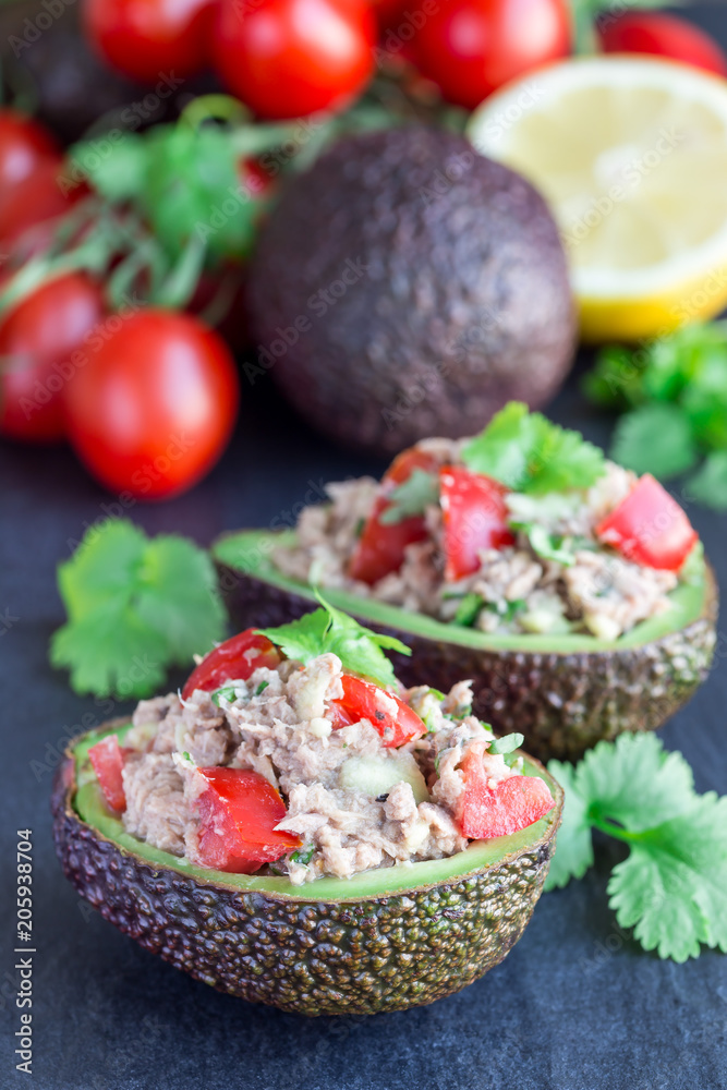 Salad with tuna, avocado, tomatos, coriander and lemon juice served in avocado bowl, ingredients on background, vertical Salad with tuna, avocado, tomatos, coriander and lemon juice served in avocado bowl, ingredients on background, vertical