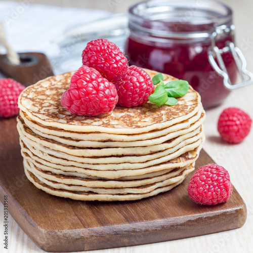 Stack of pancakes or fritters with raspberry on wooden board, raspberry jam on background, square format