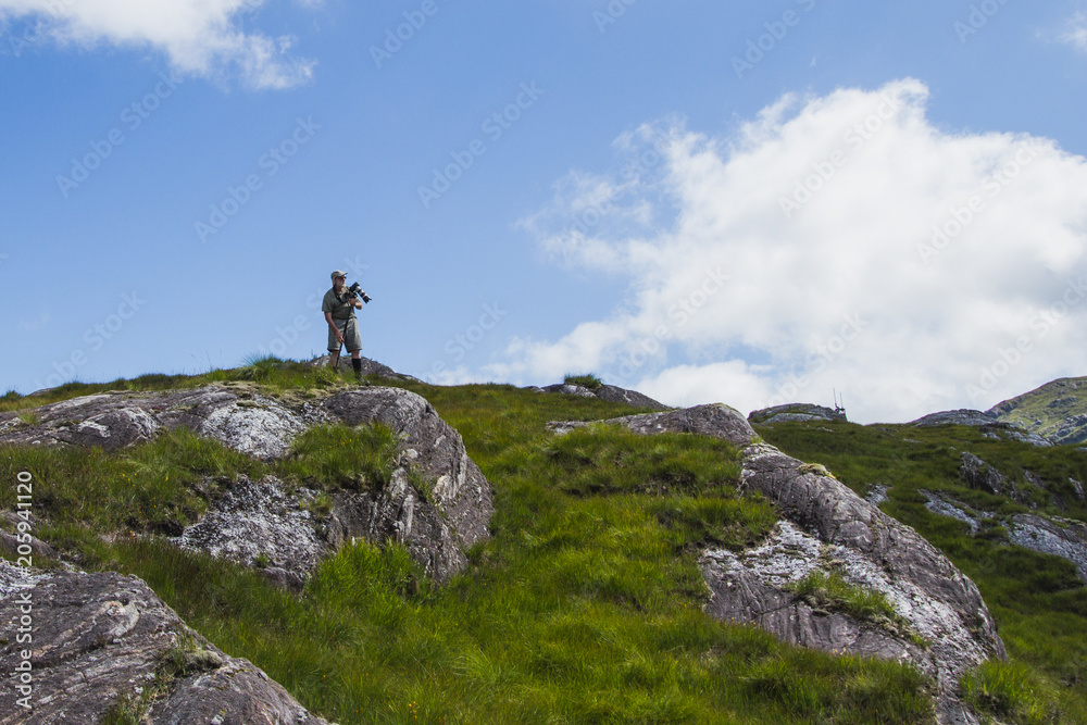 Mmature man, tourist in mountains take a picture, scottish landscape, summer
