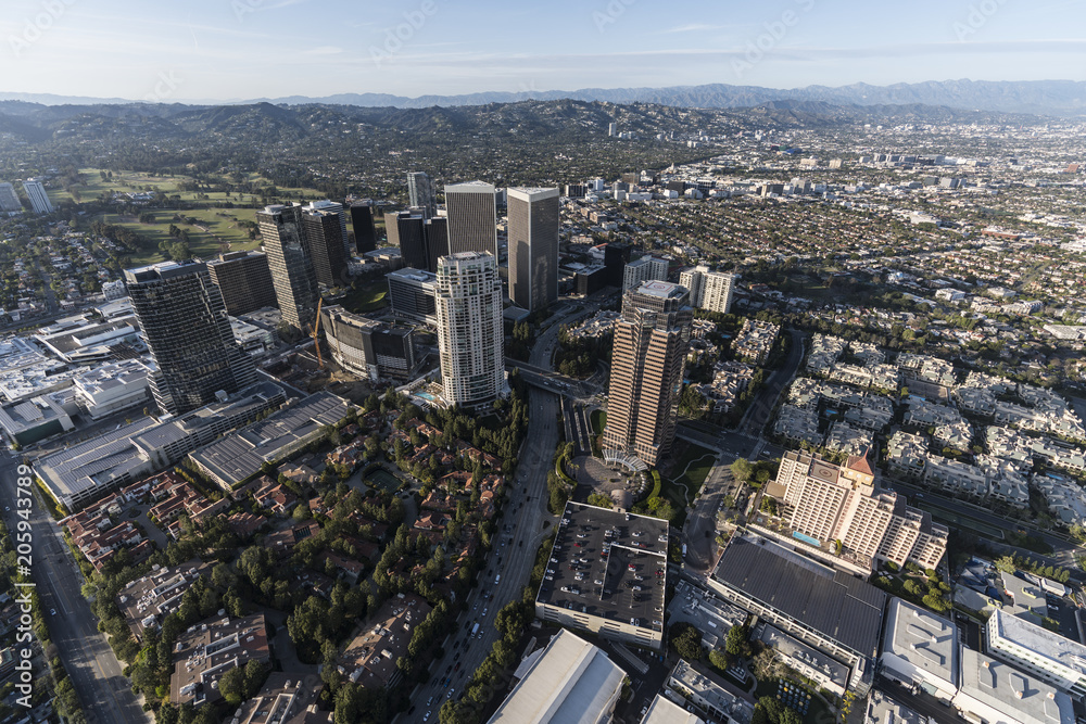 Aerial view of Los Angeles Century City towers and Olympic Bl with Beverly Hills and the Santa Monica Mountains in background.