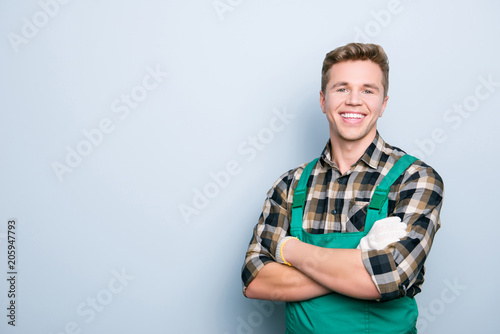 Portrait of kind cheerful excited smart professional friendly expert handsome with beaming shiny smile handyman wearing green overalls standing with folded hands isolated on gray background copyspace photo