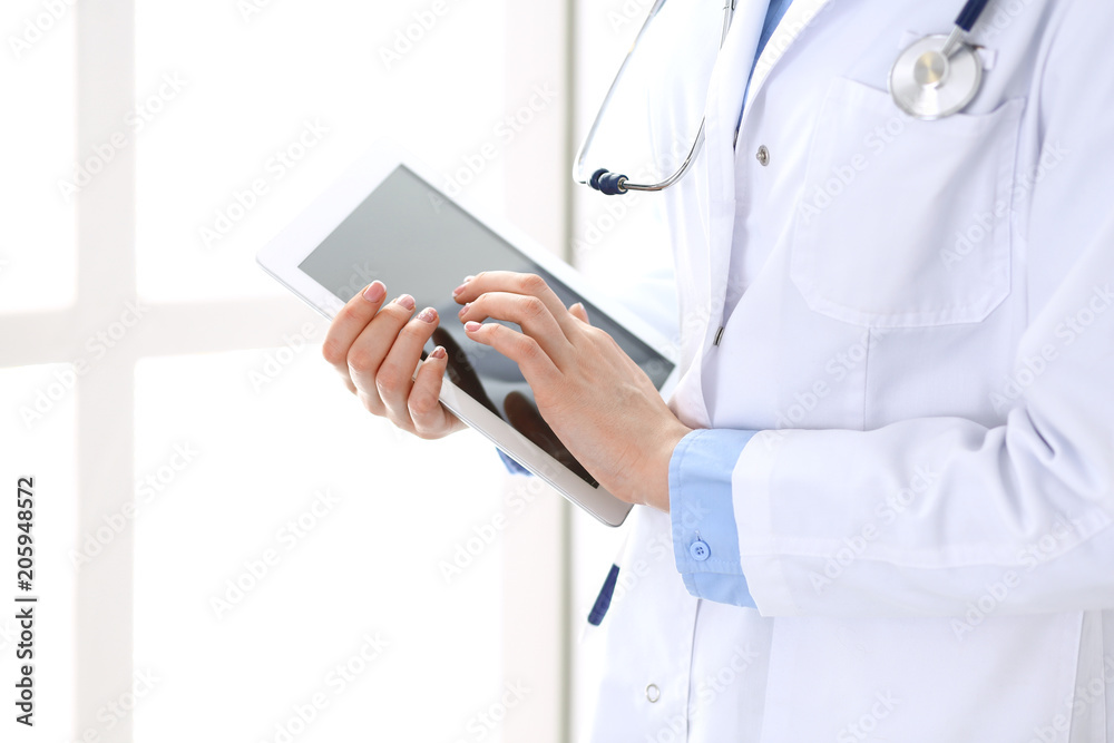 Woman doctor using tablet computer while standing straight in hospital closeup. Healthcare, insurance and medicine concept Woman doctor using tablet computer while standing straight in hospital closeup. Healthcare, insurance and medicine concept