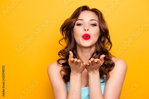 Portrait of lovely sweet girl with modern hairdo blowing air kiss with pout lips two palms at camera isolated on yellow background demonstrate feelings to her boyfriend