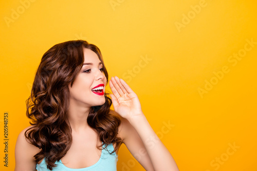 Portrait with copyspace empty place of pretty half-turned girl looking away holding palm near mouth calling someone shouting news information isolated on yellow background advertisement concept