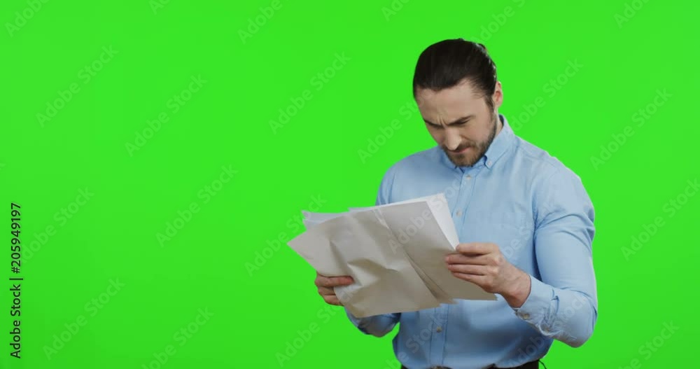 Portrait shot of the attractive Caucasian angry man in the blue shirt holding paper sheets and documents, then throwing them as being nervous. Green screen. Chroma key Portrait shot of the attractive Caucasian angry man in the blue shirt holding paper sheets and documents, then throwing them as being nervous. Green screen. Chroma key