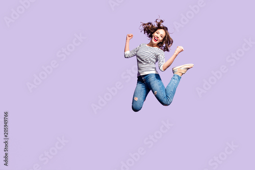 Portrait of successful crazy girl celebrating victory jumping in the air with raised fists yelling isolated on violet background, full of energy people in action concept
