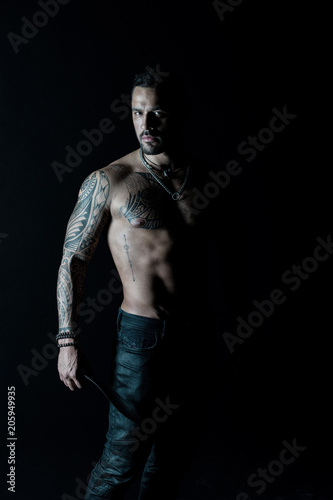 Athlete or sportsman with muscular chest and belly. Tattoo model with six pack and ab. Bearded man with tattooed body. Man with sexy bare torso in jeans. Sport or fitness and bodycare