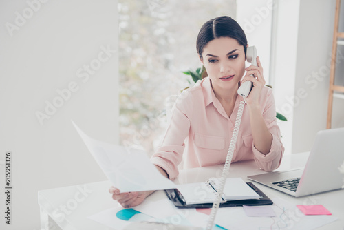 Concentrated secretary classic elegant financier making consultation looking at document in hand agent talking on telephone with partner consulting sitting in modern white office expertising analyzing photo