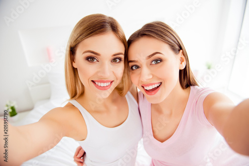 Self portrait of pretty, charming, confident, successful, cute, attractive, cheerful, girls in white and pink outfit shooting selfie on front camera with arms, sitting on bed, having good mood