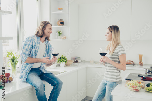 Portrait of happy cheerful partners discussing news sharing gossips in modern white kitchen while preparing dinner lunch enjoying time together