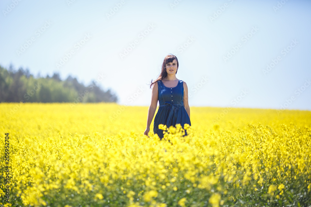 young happy beautiful  girl in a blue dress on blooming rapeseed field in summer.