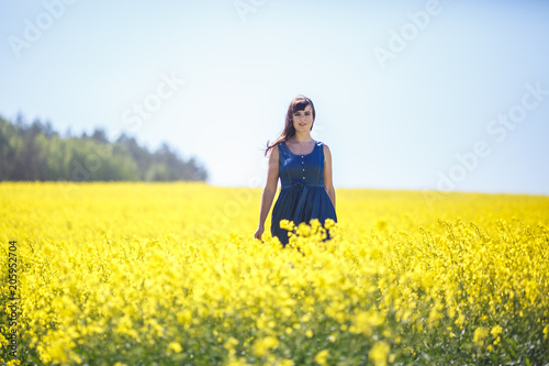 young happy beautiful  girl in a blue dress on blooming rapeseed field in summer.