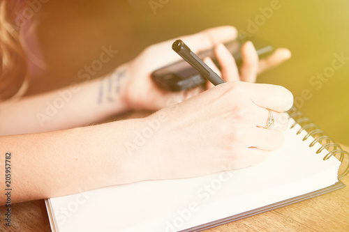 Charming young woman making notes and using mobile phone. Visual effects. Blurred background