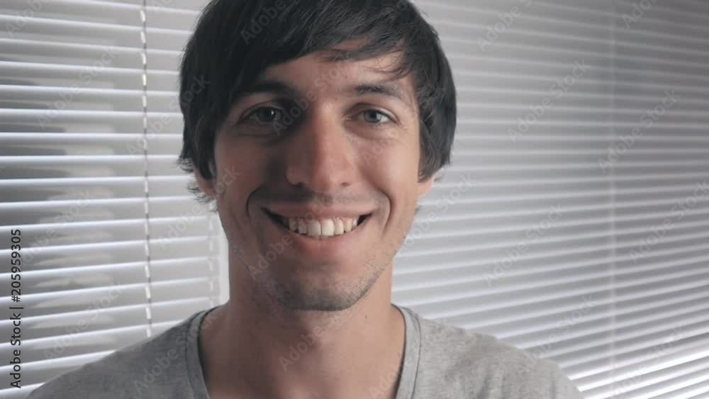 portrait of positive young man smiling against the background of office blinds portrait of positive young man smiling against the background of office blinds