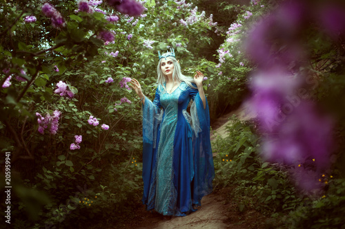 Beautiful elf woman walks in a fairy forest among the lilac bushes.