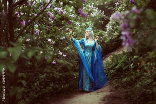 Young elf woman walks in a fairy forest among the lilac bushes.