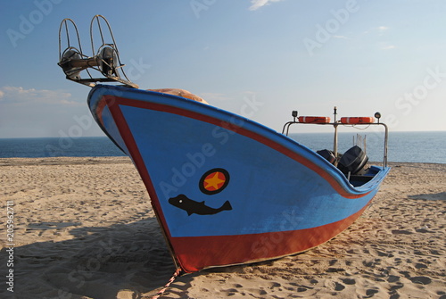 Barco de pesca parado na areia da praia, com cores azuis e vermelhos acastanhados photo