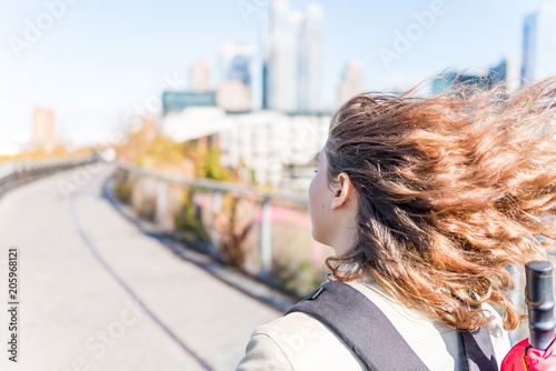 NYC in highline, high line, urban with people tourists woman walking with backpack, umbrella Chelsea West Side by Hudson Yards in autumn fall yellow golden trees, windy wind blowing hair photo