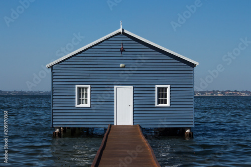 Blue wooden boatshed surrounded by water against clear blue sky