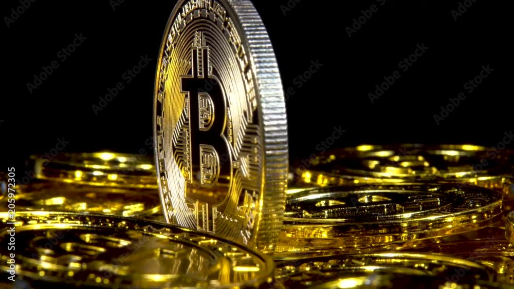 Fast rotation low angle extreme closeup of a Bitcoin amid a sea of bitcoins on a black background.
