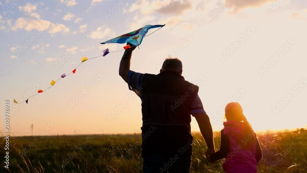 Silhouette of a happy family playing a kite. Grandpa and little girl are playing at sunset with a kite.