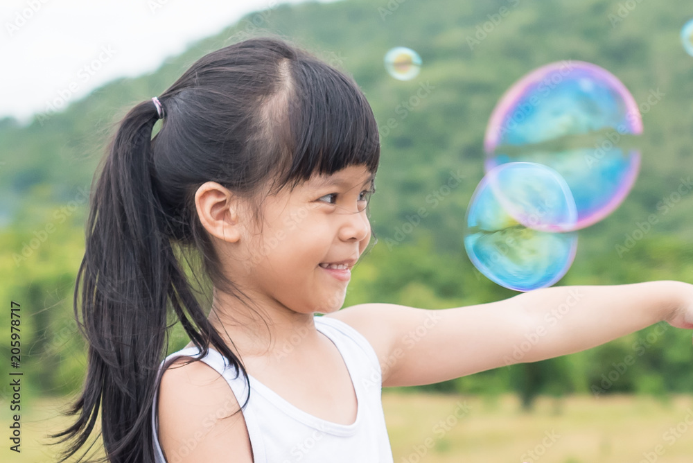 A little girl blowing soap bubbles in summer park. Background toninf for instagram filter. A little girl blowing soap bubbles in summer park. Background toninf for instagram filter.