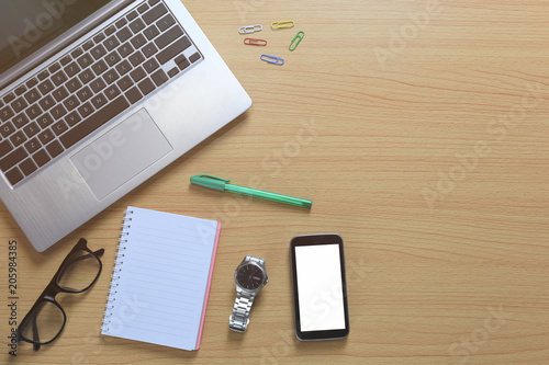 Laptop placed near a empty notebook and blank smartphone on a brown wooden floor.