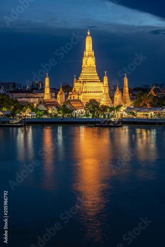 Wat Arun Temple beside Chao Phraya River at twilight time in Bangkok, Thailand. One of the most famous place of Thailand's landmarks. Light reflection on smooth water. © Opman