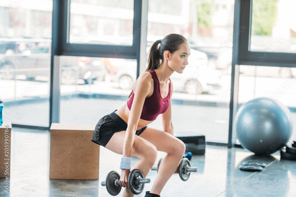side view of asian sportswoman exercising with dumbbells at gym side view of asian sportswoman exercising with dumbbells at gym