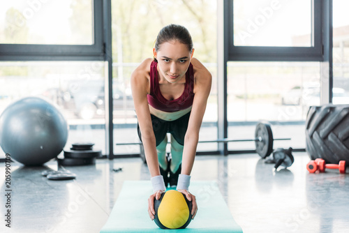 young asian sportswoman balancing on ball on fitness mat at gym