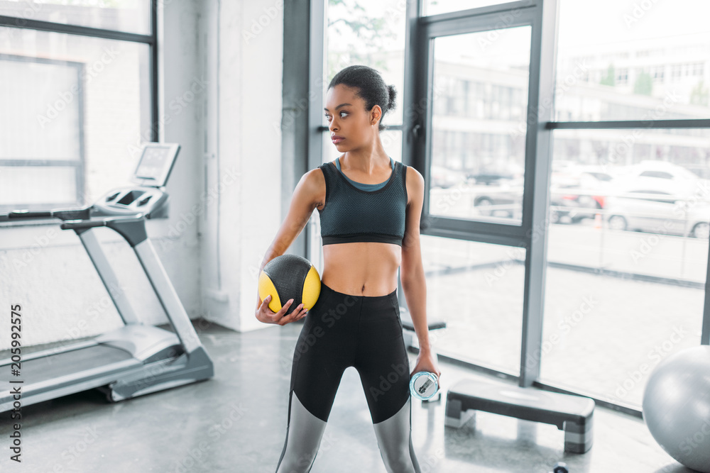 portrait of african american sportswoman with ball and sportive water bottle at gym