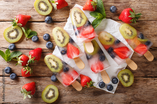Freshly prepared popsicles ice with fresh strawberries, kiwi and blueberries on a stick close-up. horizontal top view