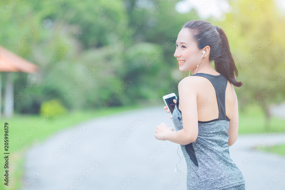 portrait of a young asian woman doing outdoor exercise in park, She ran and listened to music from a mobile phone happily.
