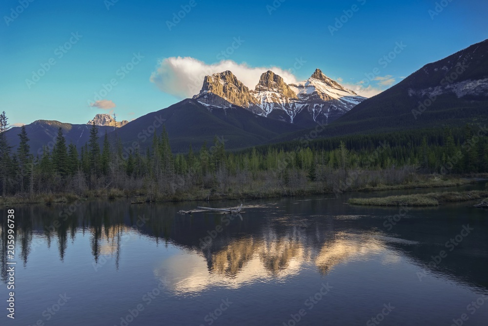 Scenic Landscape View of Snowcapped Three Sisters Mountain reflected in calm water, Alberta Foothills Canadian Rockies