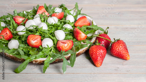 Delicious rucola salad with mozzarella and strawberries on a wooden background. Healthy foods. Banner photo