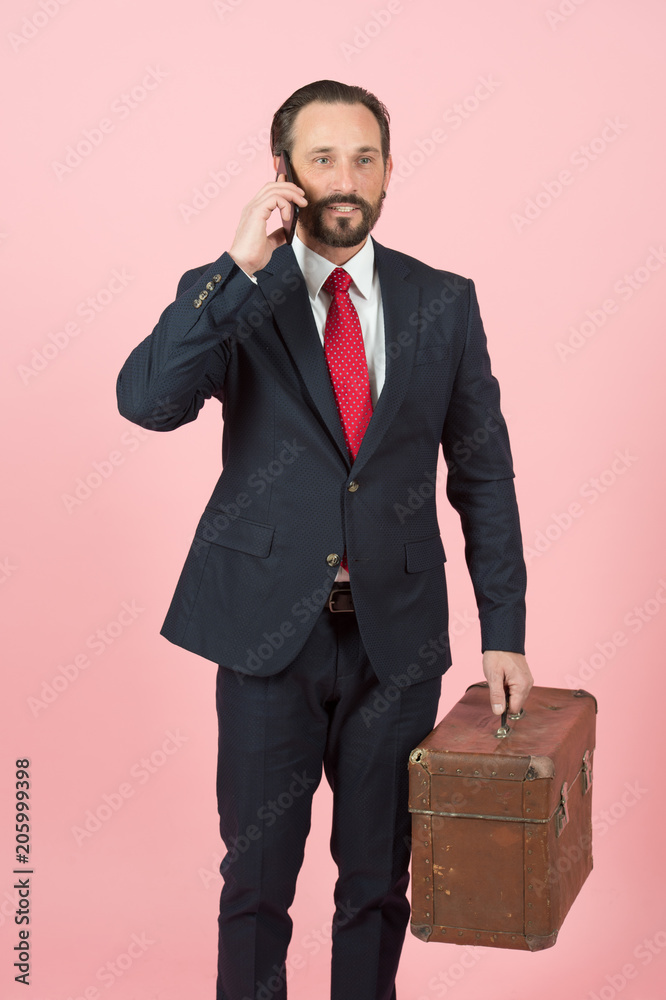 happy businessman in black suit and red tie with vintage briefcase talking over phone on pink wall background. happy businessman in black suit and red tie with vintage briefcase talking over phone on pink wall background.