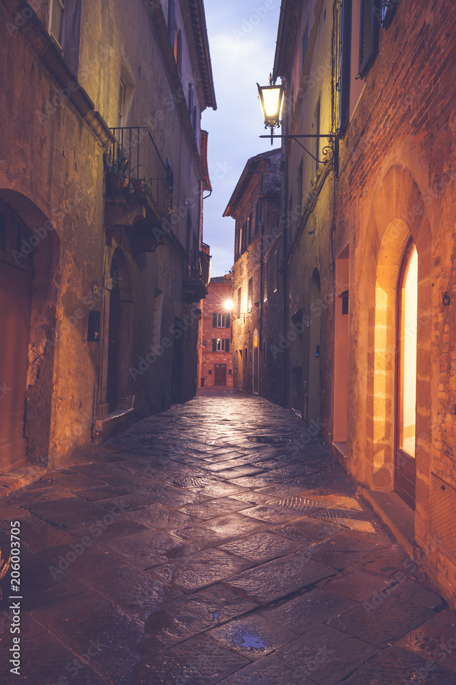 Old European narrow empty street of a medieval town at a foggy evening. Pienza, Italy