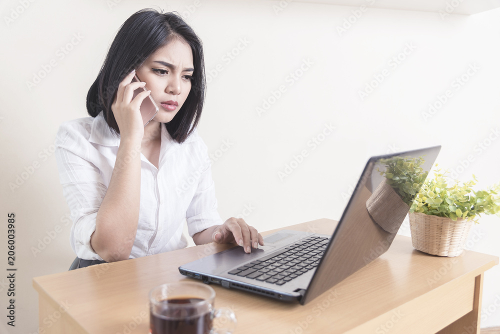 Businesswoman using mobile phone while using computer laptop at desk in office. Businesswoman using mobile phone while using computer laptop at desk in office.