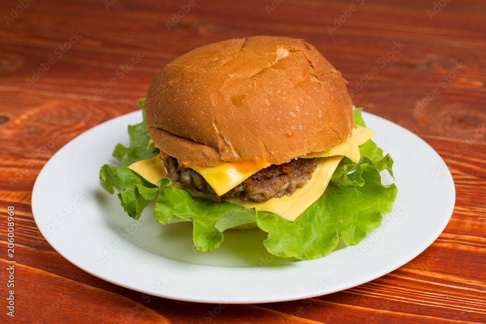 Homemade hamburger on a white plate, on a wooden table. Fast and harmful food.