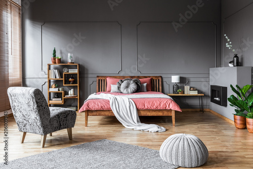 Obraz na plátně Spacious bedroom interior with pouf and gray armchair in front of a pink bed with wooden bedhead