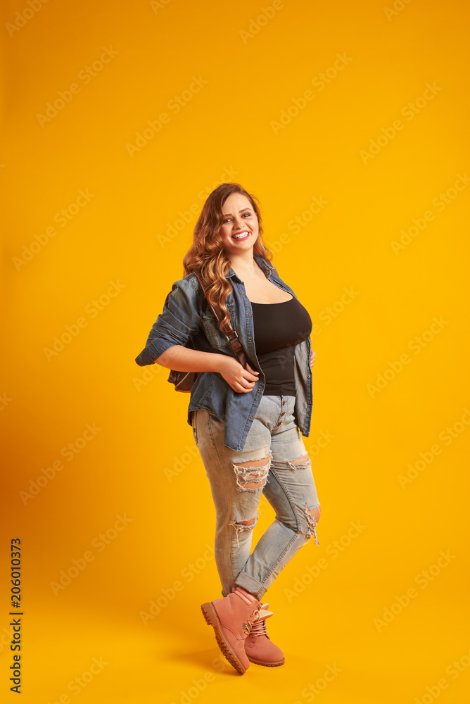 Candid curvy girl in denim jacket holding backpack and looking a Candid curvy girl in denim jacket holding backpack and looking a