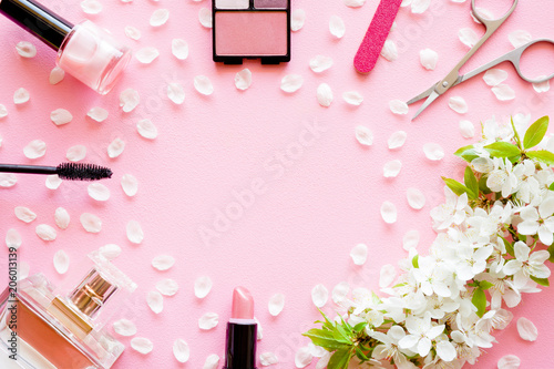 Various decorative makeup cosmetics with fresh cherry blossoms and petals on pink pastel desk. Different beauty essentials for women. Mockup for special offers as advertising. Empty place for text.