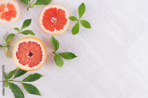 Slices grapefruit and green leaves on soft white wooden background, pattern, top view, closeup.