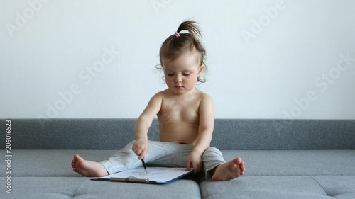 A sweet girl draws on a sheet and sits on the couch
