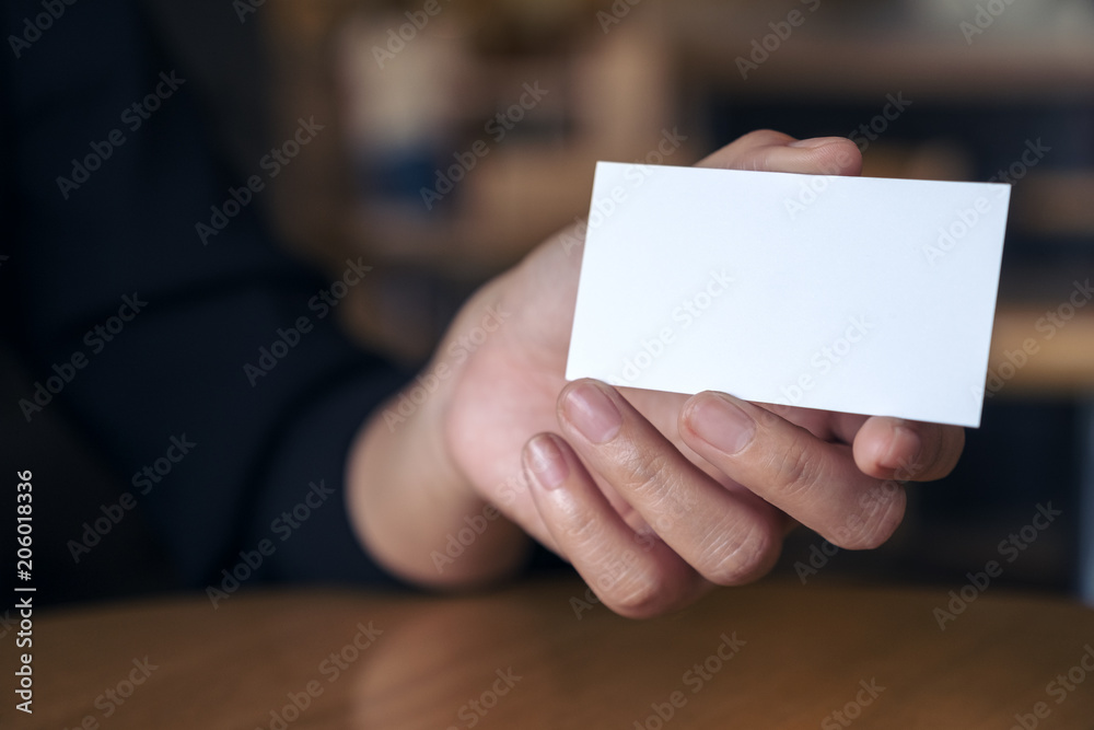 Woman's hand holding and showing an empty business card on table in office Woman's hand holding and showing an empty business card on table in office