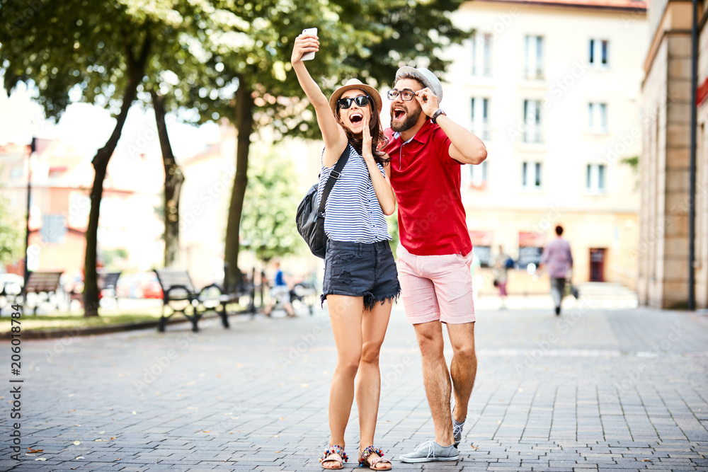 Happy couple on vacation taking selfie on city street