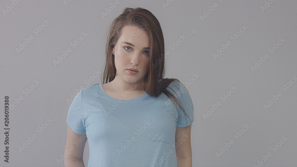 closeup portrait of young wooman posing to a camera with blowed out hair on grey