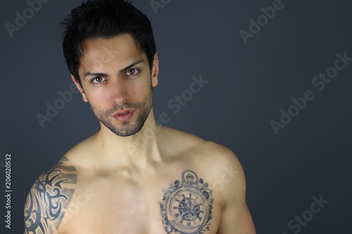 Bel homme tatoué posant sur un fond gris 