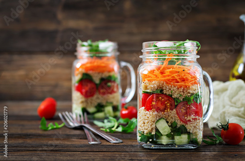 Salads with quinoa, arugula, radish, tomatoes and cucumber in glass jars on wooden background. Healthy food, diet, detox and vegetarian concept