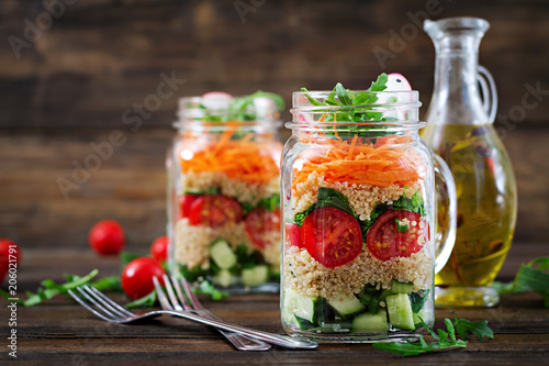 Salads with quinoa, arugula, radish, tomatoes and cucumber in glass jars on wooden background. Healthy food, diet, detox and vegetarian concept